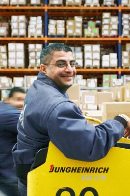 Logistik im Unternehmen: Mitarbeiter auf Hubwagen vor Hochregal 
